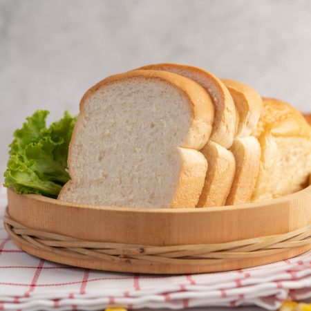 Bread in a wooden tray on a red and white cloth with lettuce and corn.