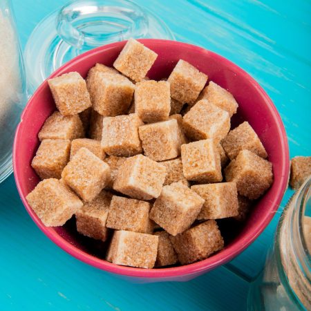 side view of brown sugar cubes in a pink bowl on blue wooden background